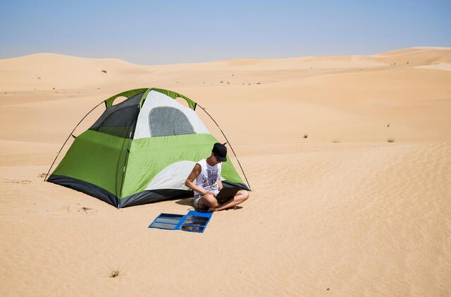 person in the desert with a camping tent and laptop with flexible solar panel