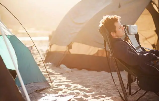 relaxed man in a camping shair on a beach at morning